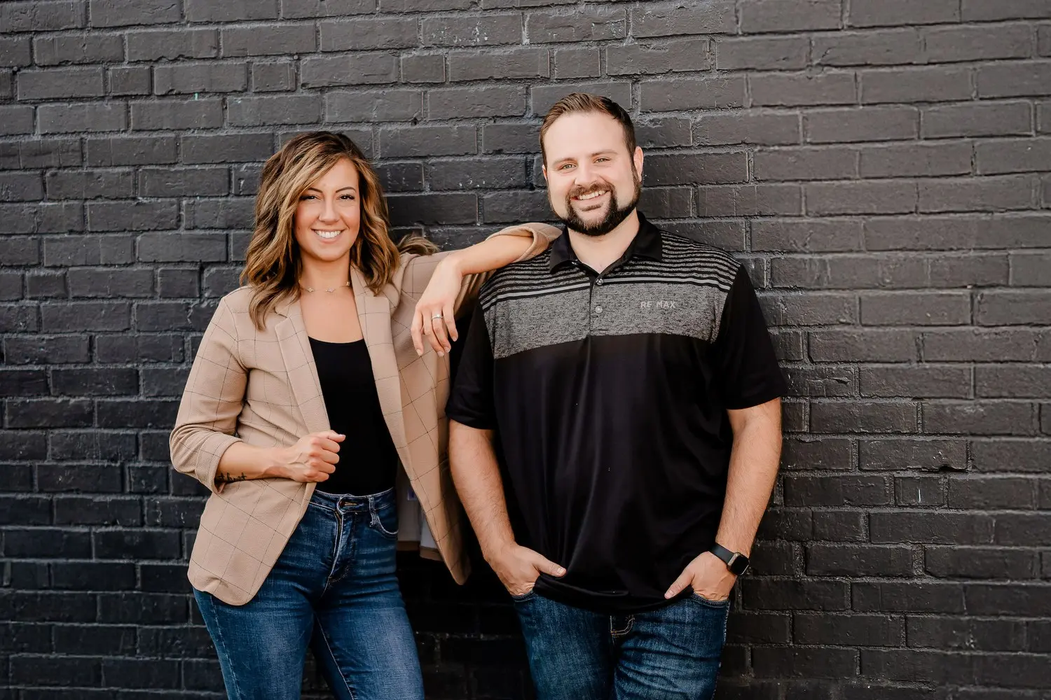 Austin Moore and Ashley Milton standing together beside a dark brick wall